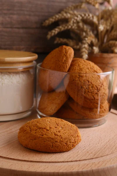 Cookies and jar of wheat flour on wooden board, closeup view