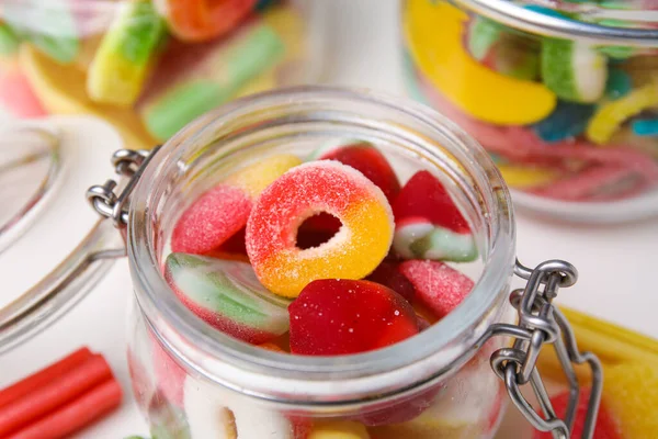 Tasty jelly candies in jars on white table, closeup