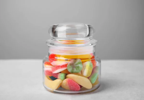 Tasty jelly candies in jar on light grey table, closeup