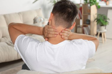 Man suffering from neck pain indoors, back view