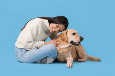 Açık mavi arka planda şirin Labrador Retriever ile oynayan mutlu kadın.