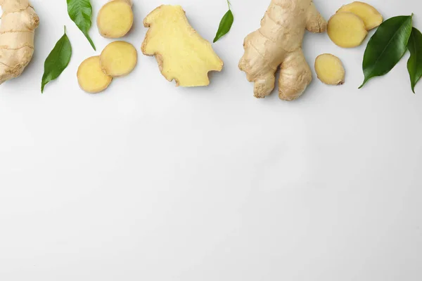 Fresh ginger with green leaves on white background, flat lay. Space for text