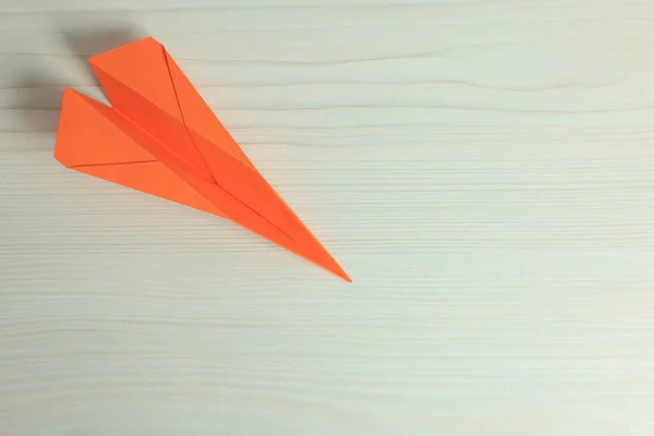 Handmade orange paper plane on beige wooden table, top view. Space for text
