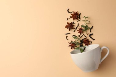 Anason yıldızları, kuru çay ve nane şekeri bej arka planda fincanın içine düşüyor. Metin için boşluk