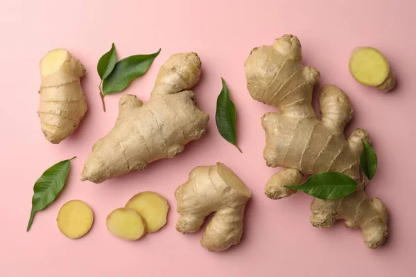 Fresh ginger with green leaves on pale pink background, flat lay