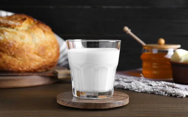Glass with fresh milk, honey and bread on wooden table