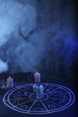 Zodyak işaretleri için doğal taşlar, çizilmiş astroloji çizelgesi ve koyu mavi masa üzerinde yanan mumlar, metin için alan