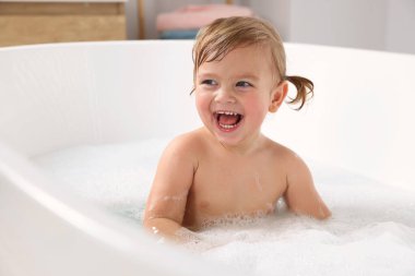 Şirin küçük kız evde köpüklü banyo yapıyor.