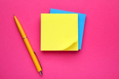 Renkli boş notlar ve pembe arkaplandaki kalem, düz yatış