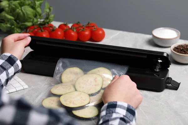 stock image Woman packing cut eggplant into plastic bag using vacuum sealer on light grey marble table, closeup