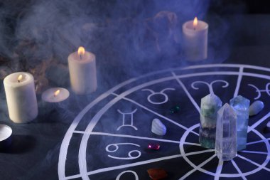 Zodyak işaretleri için doğal taşlar, astroloji çizelgesi ve siyah masada yanan mumlar. Renk tonu etkisi