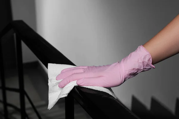 Woman in glove cleaning railing with paper towel indoors, closeup