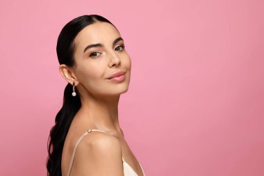 Pembe arka planda zarif inci küpeler takan genç bir kadın.