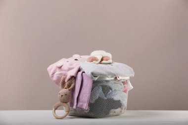 Bebek kıyafetleri ve beyaz ahşap masada oyuncak dolu çamaşır sepeti.