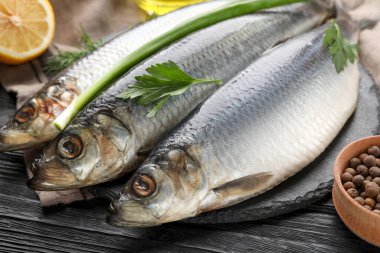 Lezzetli tuzlu ringa balıkları ve siyah ahşap masa üzerindeki malzemeler, yakın plan.