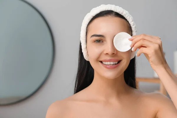 Young woman using cotton pad with micellar water indoors