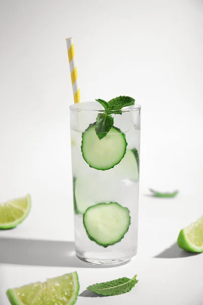 Glass of tasty fresh cucumber water with mint and sliced lime on white background