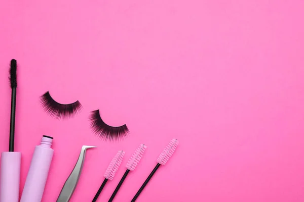 Fake eyelashes, brushes and tweezers on pink background, flat lay. Space for text