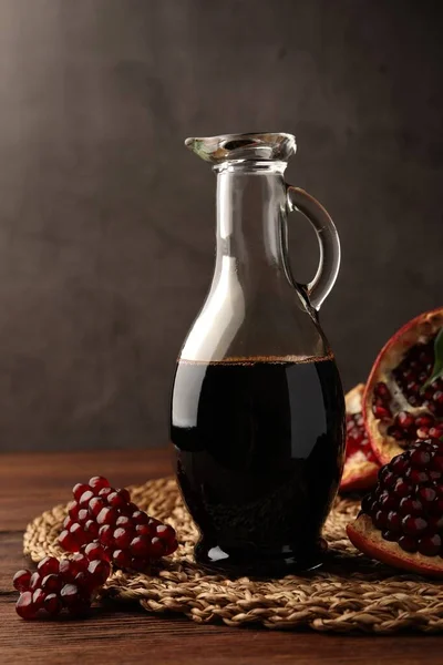 Glass jug of tasty pomegranate sauce and fresh ripe fruit on wooden table