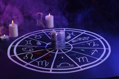 Zodyak işaretleri için doğal taşlar, astroloji çizelgesi ve koyu mavi masada yanan mumlar. Renk tonu etkisi