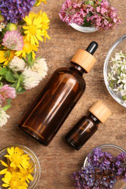 Ahşap masa üzerinde güzel çiçeklerle çevrili gerekli yağlardan oluşan şişeler.