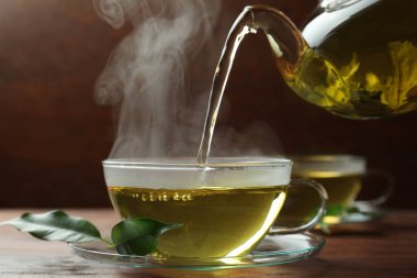 Yeşil çayı çay bardağına çay tabağı ve yapraklarla dolduruyor, yakın plan.