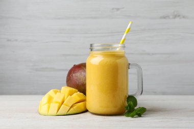 Lezzetli meyve püresi ve beyaz ahşap masada taze mango ile mason kavanozu.