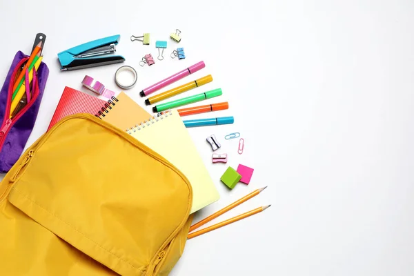 Backpack with different school stationery on white background, flat lay. Space for text