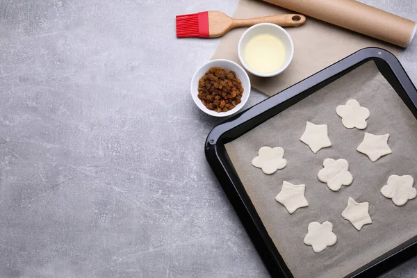Parchment paper, baking pan with raw cookies and different ingredients on light grey table, flat lay. Space for text