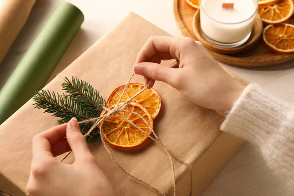 Woman decorating gift box with dry orange slices at white wooden table, closeup
