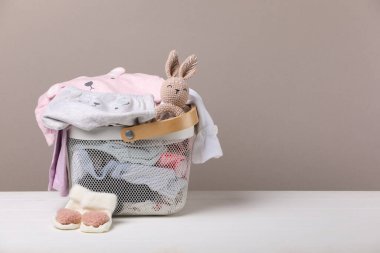 Beyaz ahşap masa üzerinde bebek kıyafetleri olan çamaşır sepeti, metin için yer.