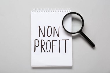 Kâr amacı gütmeyen ve açık gri zemin üzerinde büyüteç olan not defteri, düz yatıyordu