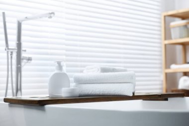 Stacked bath towels and personal care products on tub tray in bathroom
