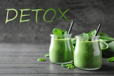 Gri ahşap masada sağlıklı yeşil ıspanaklı smoothie kavanozları ve kelime Detox