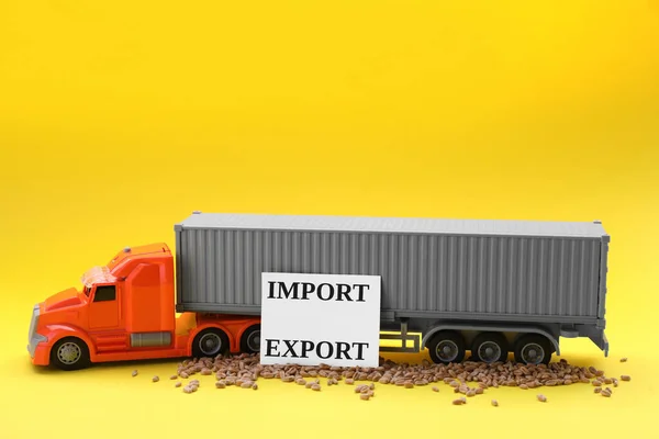 Card with words Import and Export, wheat grains near toy truck on yellow background