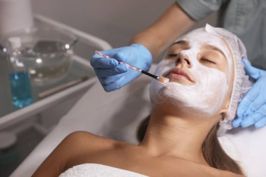 Spa salonu müşterinin yüzüne maske uygulayarak güzellik uzmanı