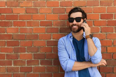 Kırmızı tuğla duvarın yanında telefonla konuşan mutlu bir adam. Metin için boşluk