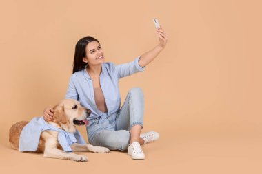 Mutlu kadın, bej arka planda şirin Labrador Retriever ile selfie çekiyor. Metin için boşluk