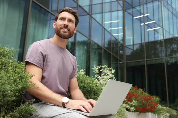 Handsome man with laptop near beautiful plants on city street