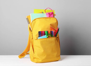 Beyaz masada gri arka planda farklı okul kırtasiyesine sahip sarı sırt çantası