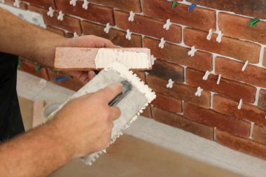 Profesyonel müteahhit, duvarın yanındaki dekoratif tuğlaya çimento sürüyor. Yakın plan. Döşeme kurulum süreci