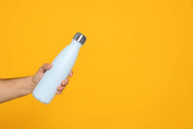 Turuncu arka planda termosu olan bir adam, yakın plan. Metin için boşluk