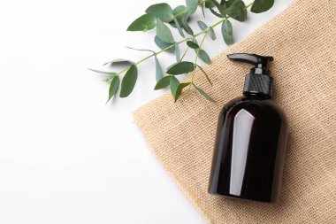 Beyaz arka planda şampuan şişesi ve yeşil yapraklar. Metin için boşluk