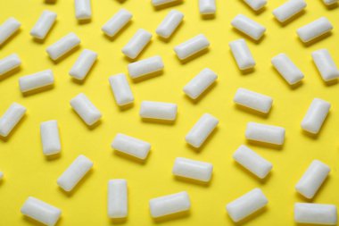 Sarı arka planda dişetleri çiğneyen lezzetli beyaz sakızlar, düz uzanmış.