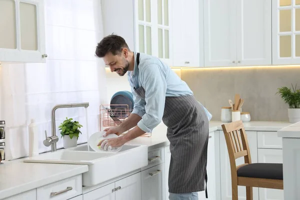 Man washing plate above sink in kitchen
