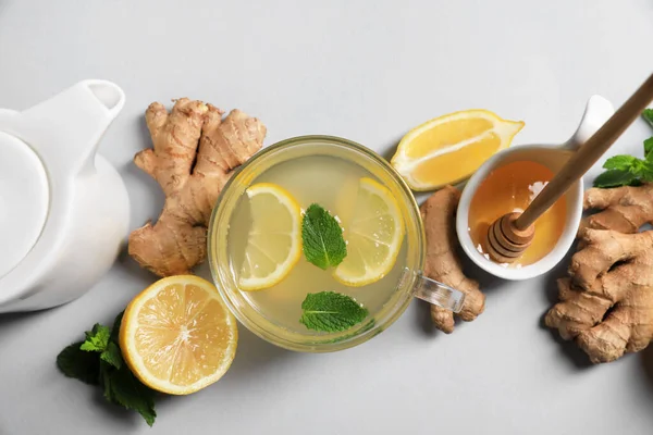 Delicious ginger tea and ingredients on light grey background, flat lay