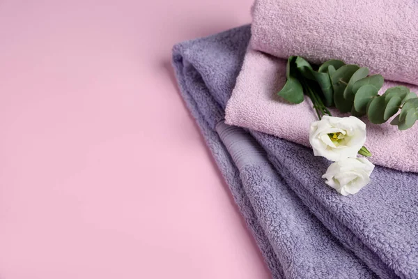 Soft folded towels with flowers and eucalyptus branch on pink background, closeup. Space for text