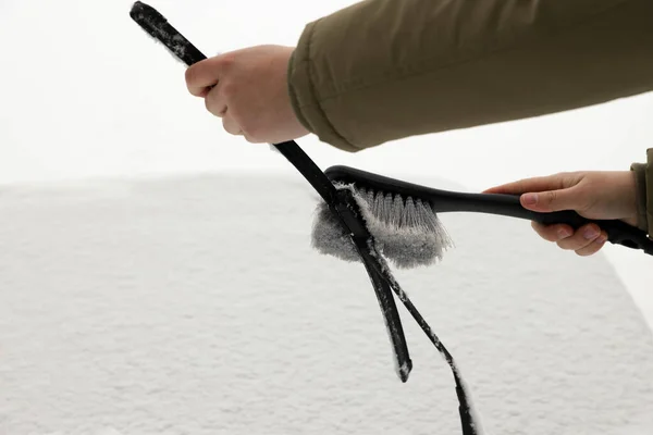 Woman cleaning car wiper blade from snow with brush, closeup