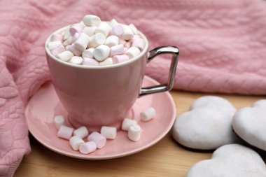 Marshmallowlu bir fincan lezzetli kakao, pembe kazak ve ahşap masada kurabiyeler.