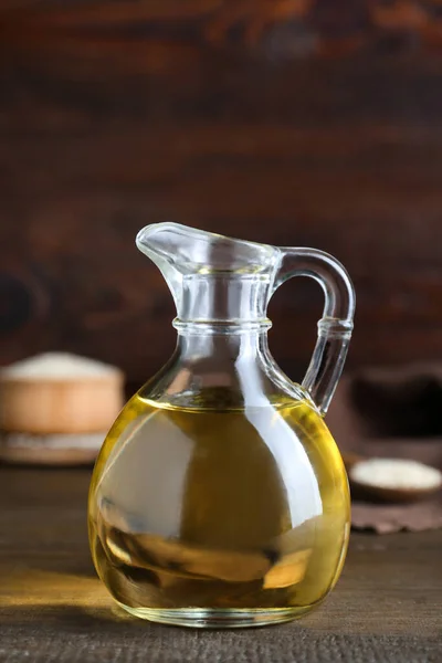 Jug of organic sesame oil and seeds on wooden table, closeup